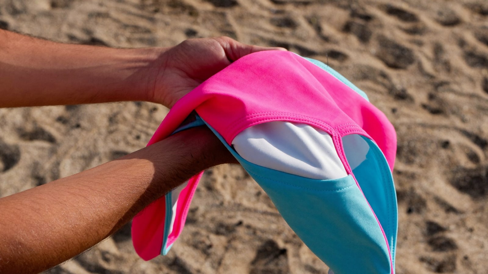 Hands holding a reversible swimsuit top showing a different colour on each side
